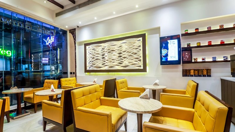 Café Brownie boutique lounge with yellow quilted armchairs, marble tables, and illuminated wave wall panel at Hotel Grand Godwin