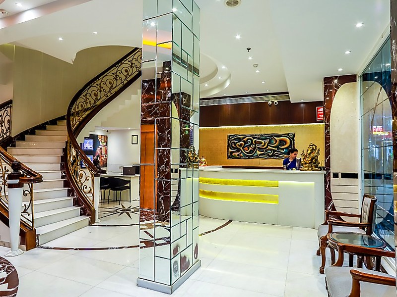 Hotel Grand Godwin New Delhi reception lobby — grand curved staircase, mirrored column, illuminated reception desk with receptionist, and golden Ganesha idol